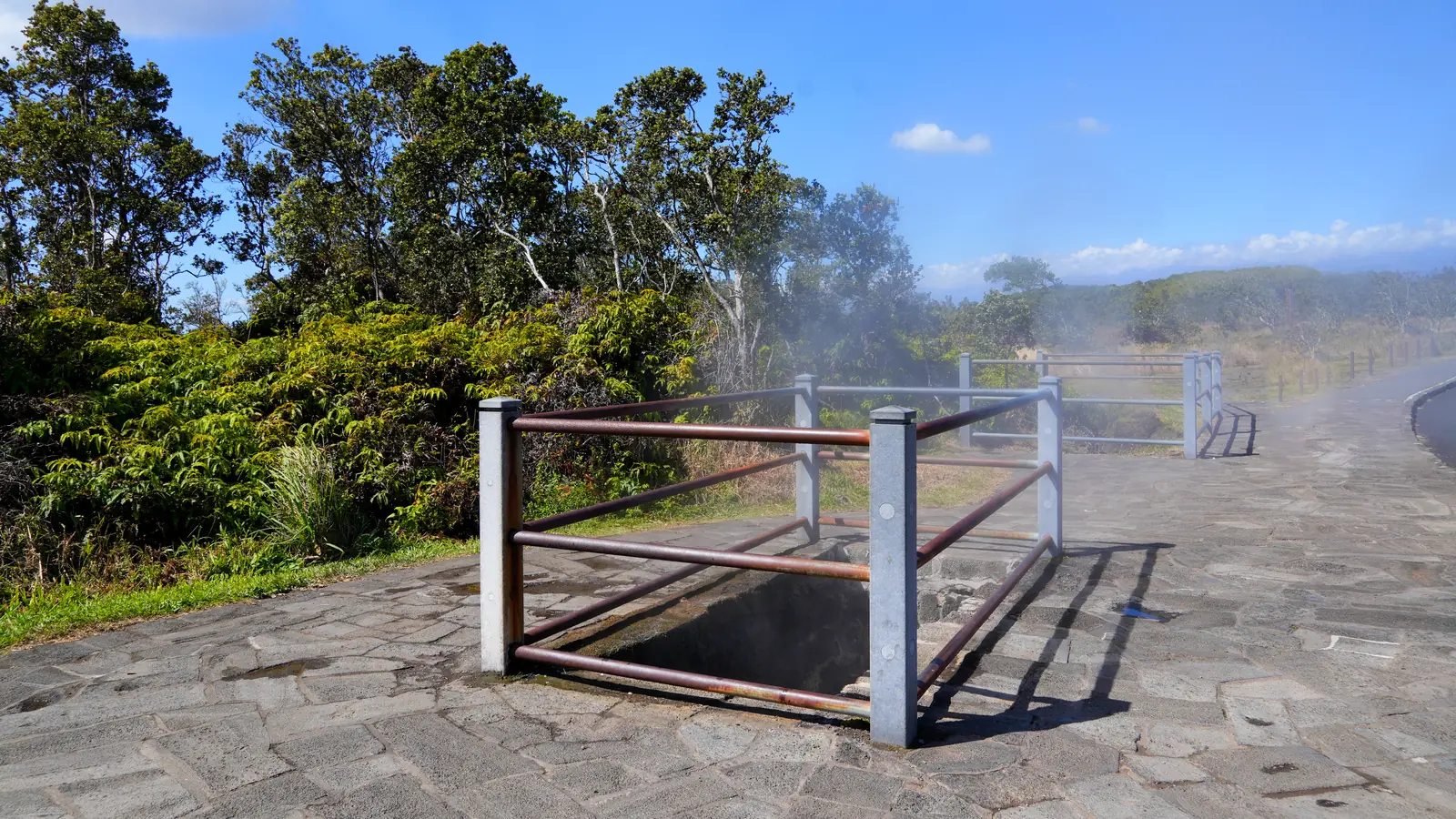 Steam rising from a railed vent beside a paved path near Kīlauea Caldera