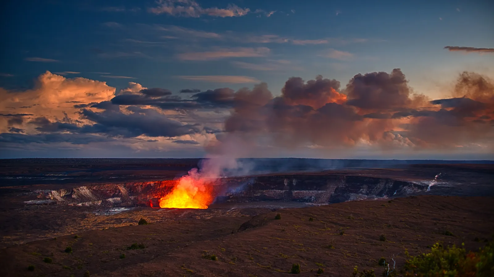 Halemaʻumaʻu Crater glowing at dusk with a steam plume rising above Kīlauea Caldera