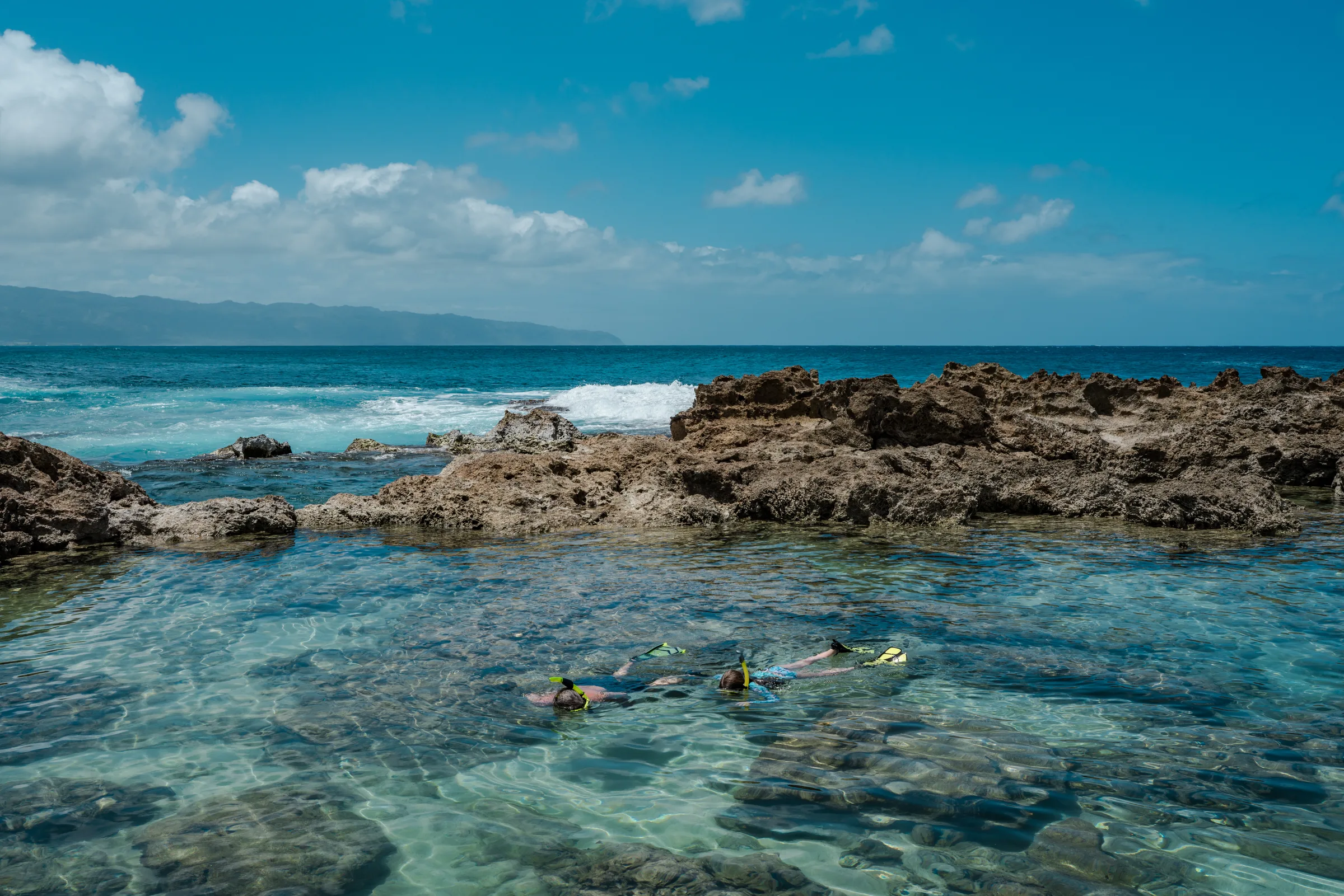Snorkelers in a calm rocky tide pool along a lava shoreline