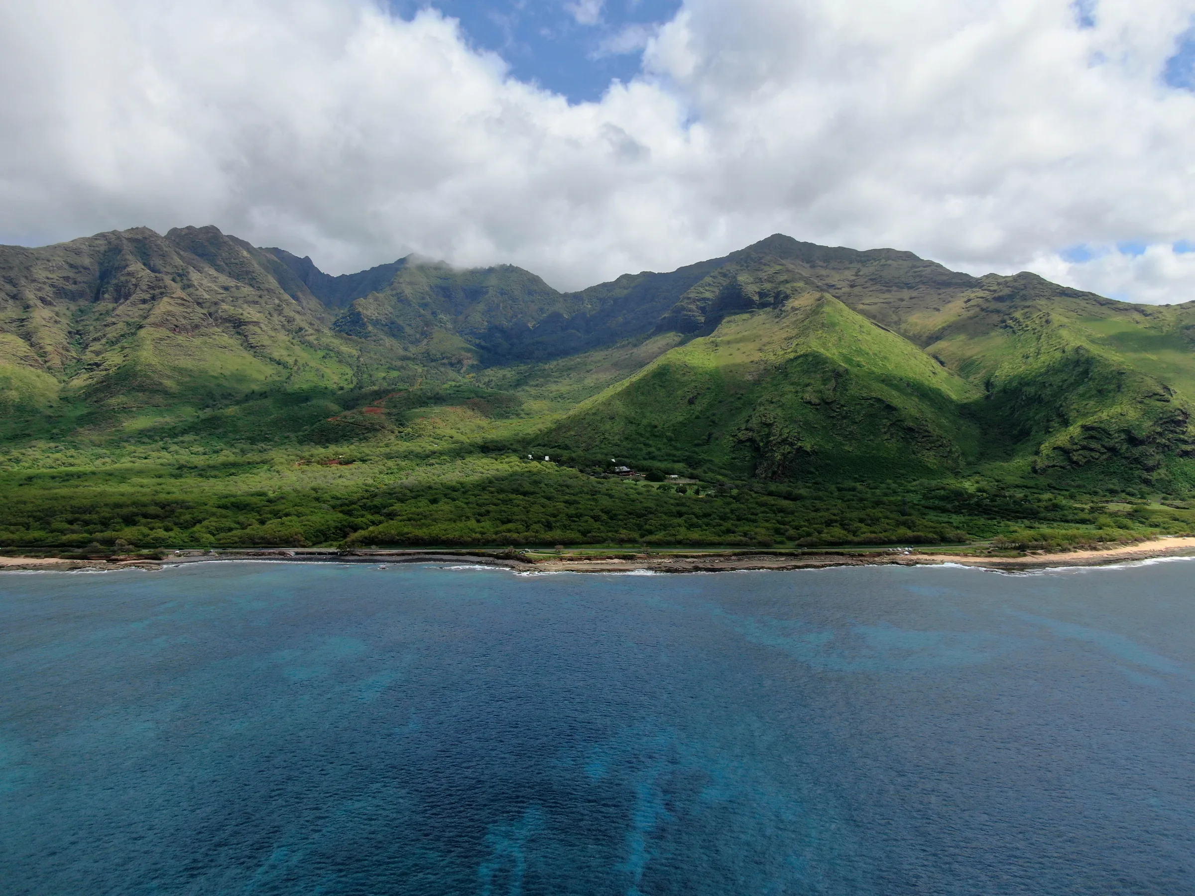 Green mountains rising behind a dry coastline above deep blue water