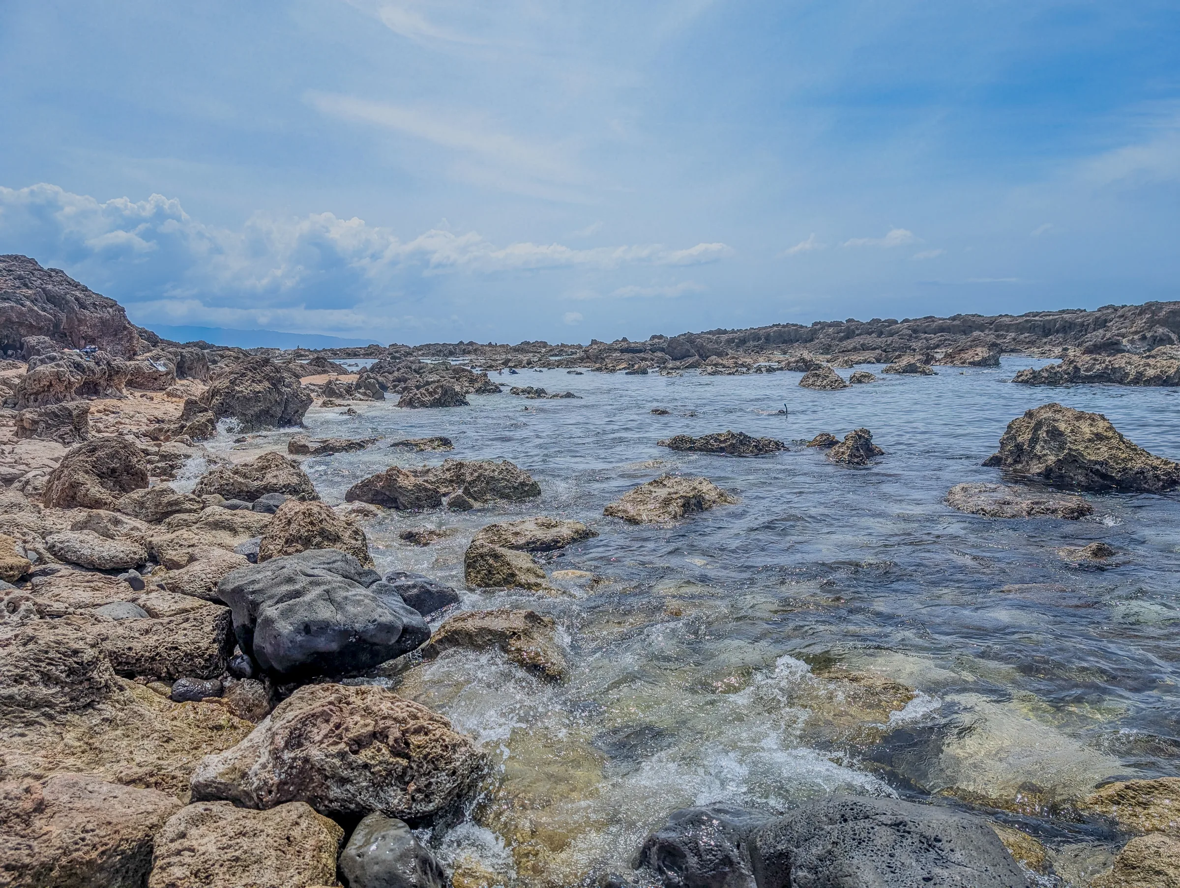 Rocky tide pools along a lava shoreline under a blue sky